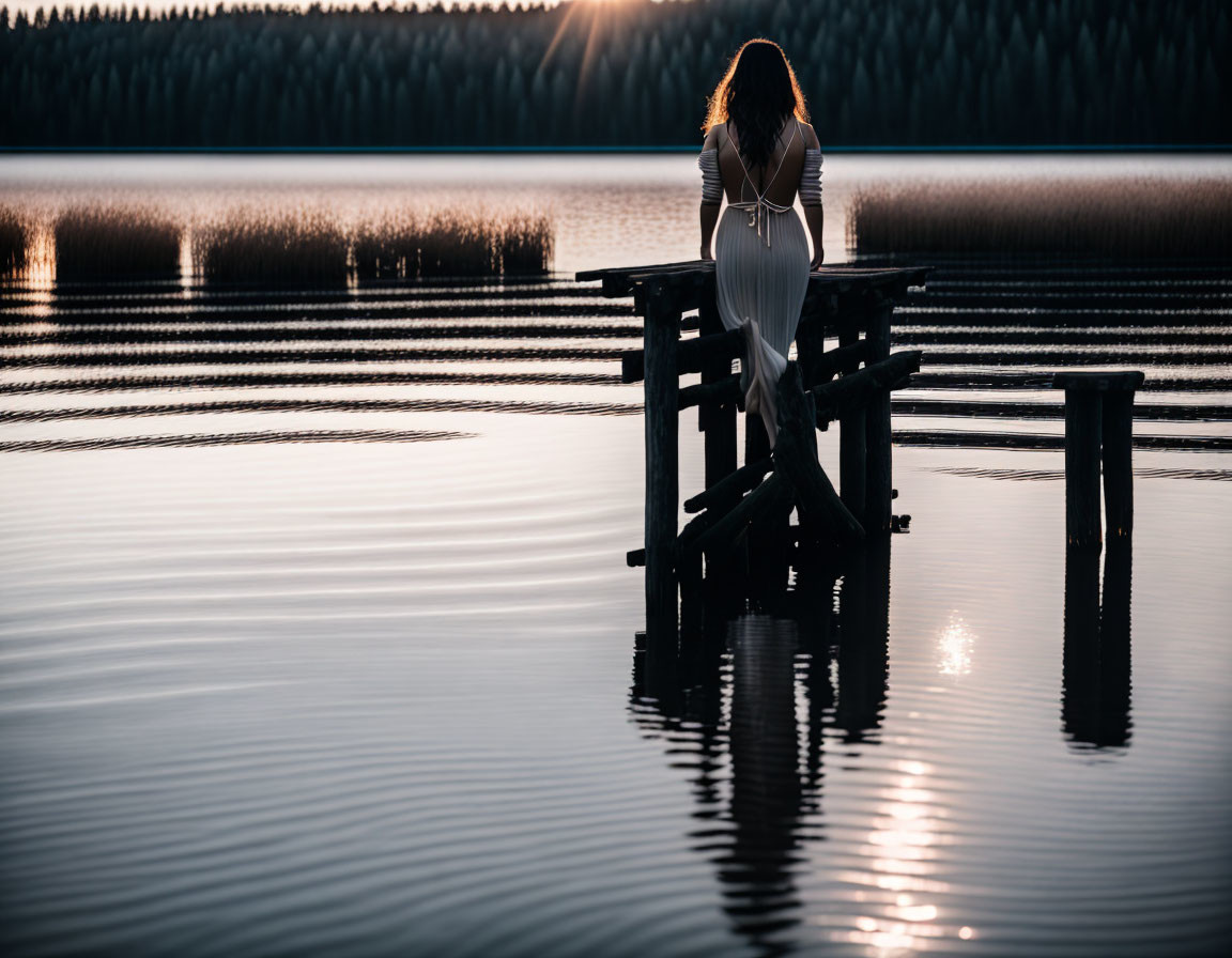 Person sitting on wooden dock by tranquil lake at sunset