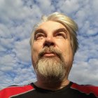 Elderly man with white beard and mustache gazing at sky with clouds