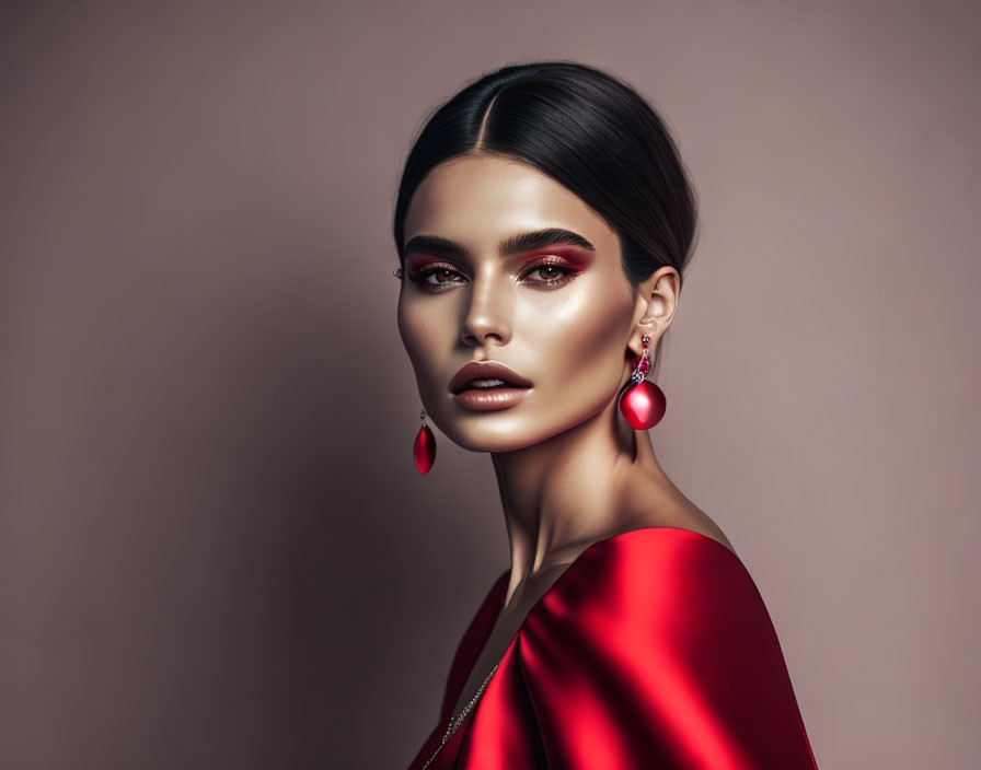 Woman with sleek hair and bold makeup in red outfit and earrings on taupe background