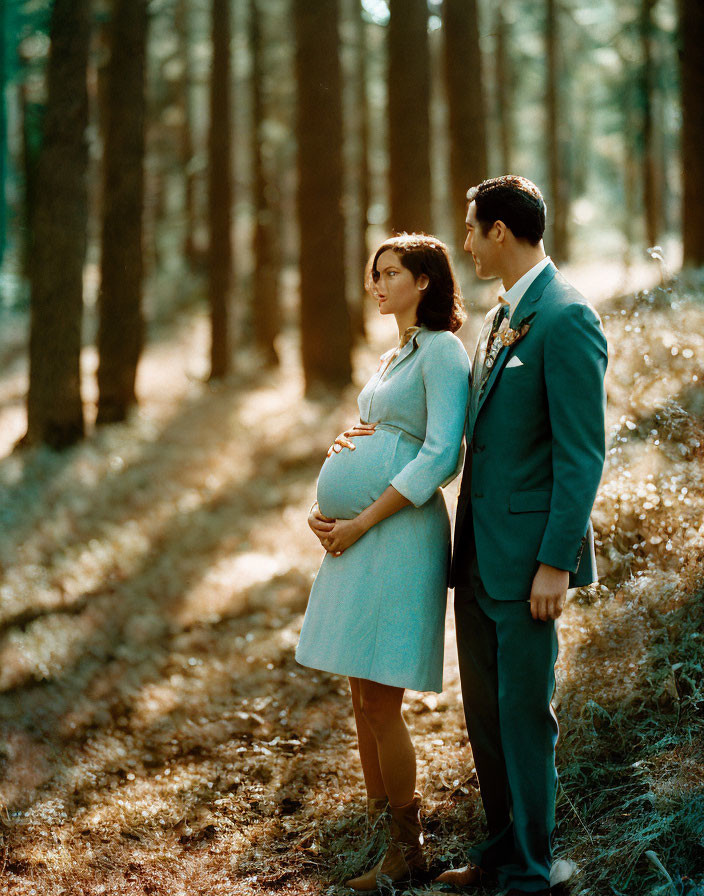 Pregnant woman and man in suit standing in sunlit forest