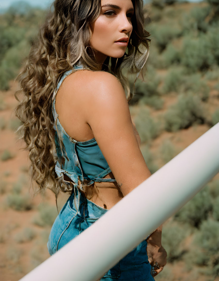 Curly-Haired Woman in Denim Top Leans on Railing with Desert Background