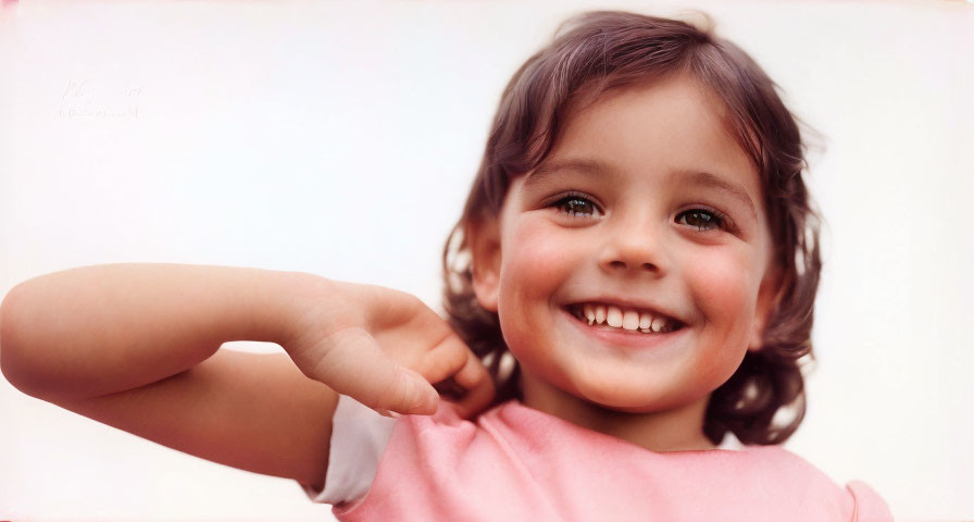 Young child with short dark hair in pink top smiling at camera