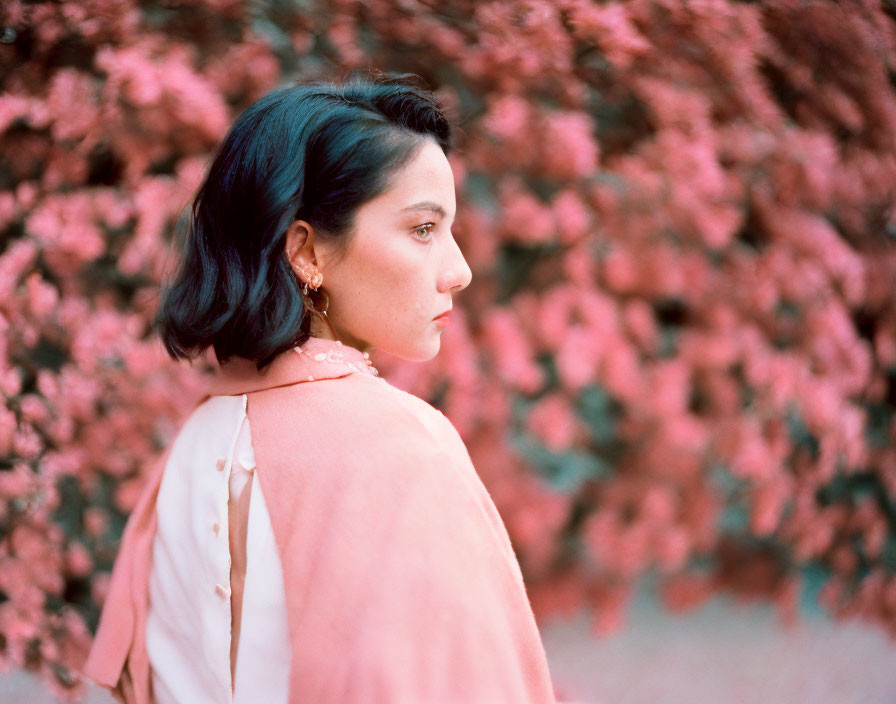 Dark-haired woman in peach shawl amid pink flowers and gold earrings