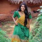 Traditional Indian woman in green and gold saree with intricate jewelry, standing in lush foliage