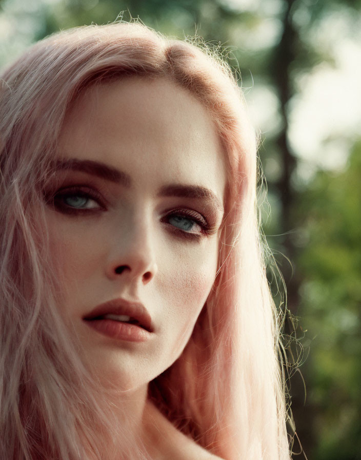 Pink-haired woman gazes thoughtfully with blue eyes, trees in soft blur.