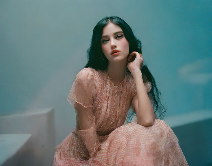 Young woman in peach lace dress seated against soft blue background