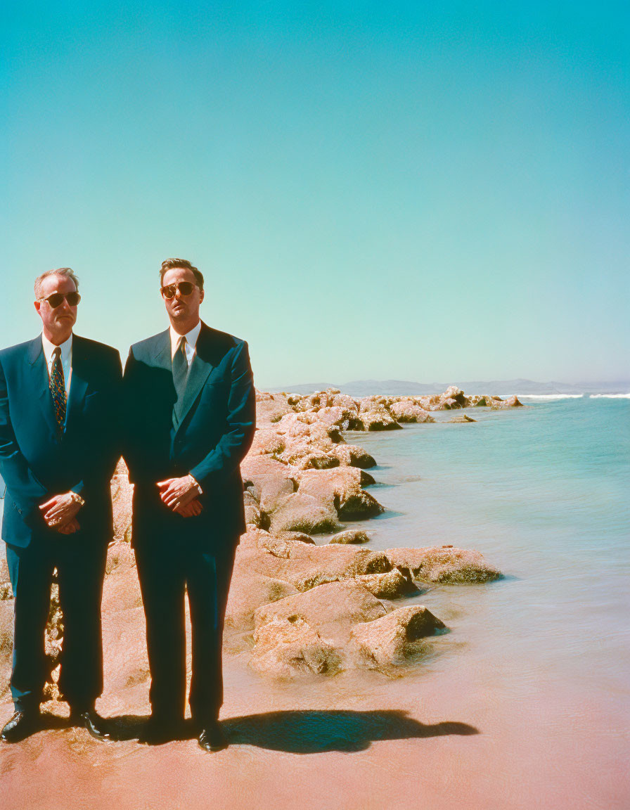 Men in suits by the sea on rocky pier under clear blue sky