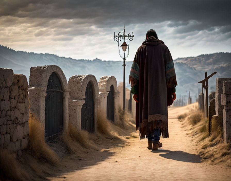 Person in poncho walking on dusty road with old walls and street lamps under cloudy sky