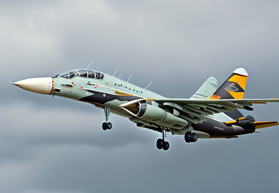 Gray military jet with yellow and black tail accents flying with missiles.