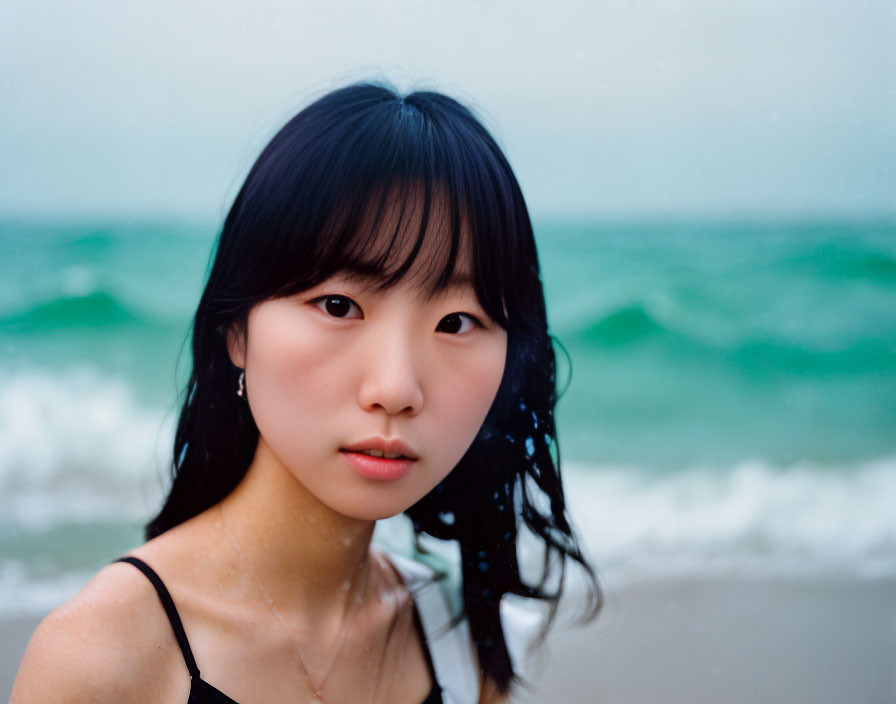 Young woman with black hair standing on beach with sea in background