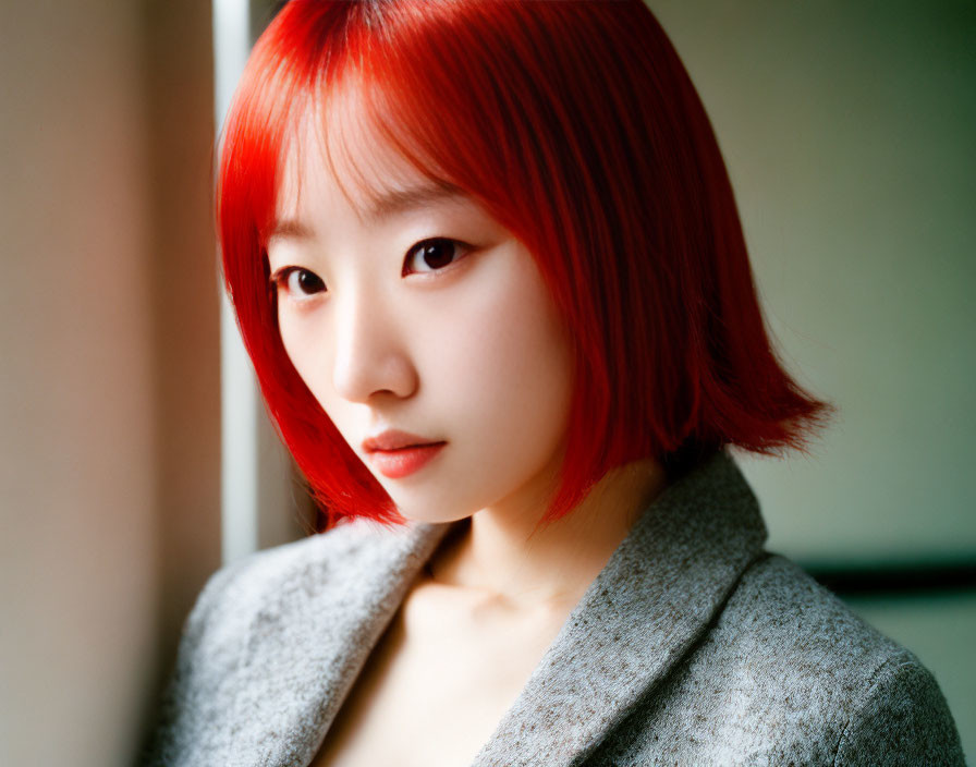 Red-haired person in gray coat gazes at camera on blurred backdrop