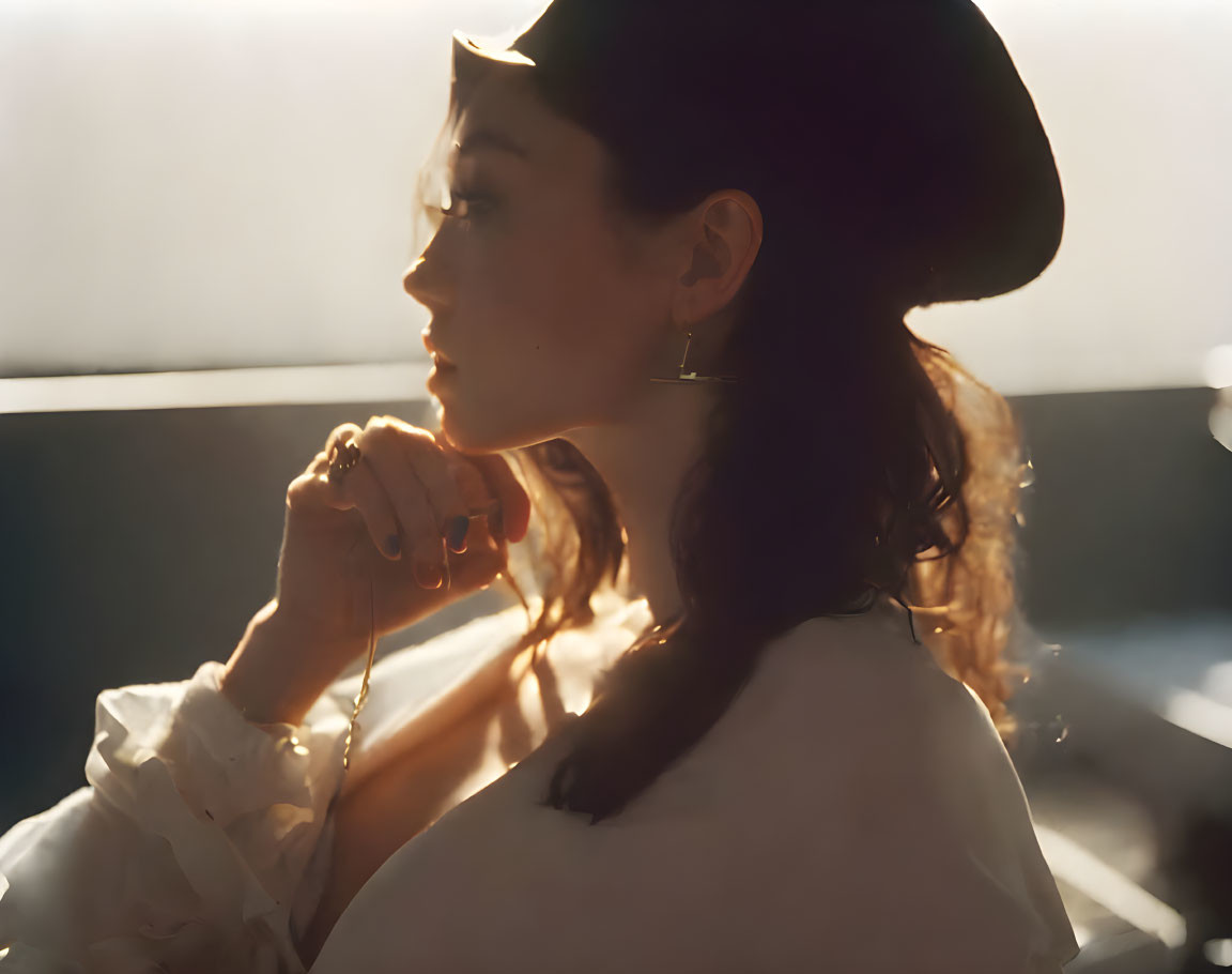 Woman in white blouse and hat under warm sunlight, gazing contemplatively.