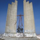 Futuristic monument with tall spire, concrete structure, red trees, blue sky