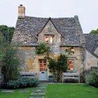 Purple wisteria-covered cottage with thatched roof and circular door in lush garden