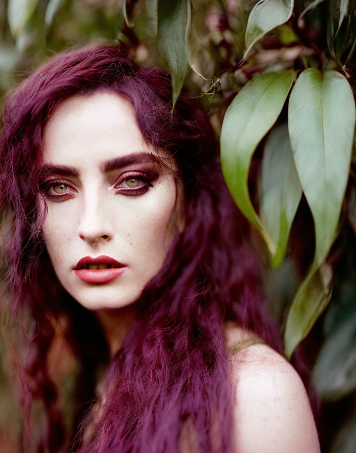 Woman with Purple Hair and Striking Makeup Surrounded by Green Leaves