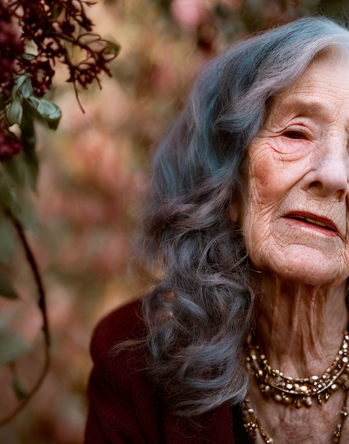 Elderly woman with gray hair in maroon outfit among autumn foliage