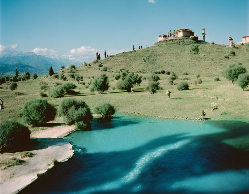 Tranquil landscape with blue river, green banks, trees, hilltop building.