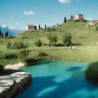 Tranquil landscape with blue river, green banks, trees, hilltop building.