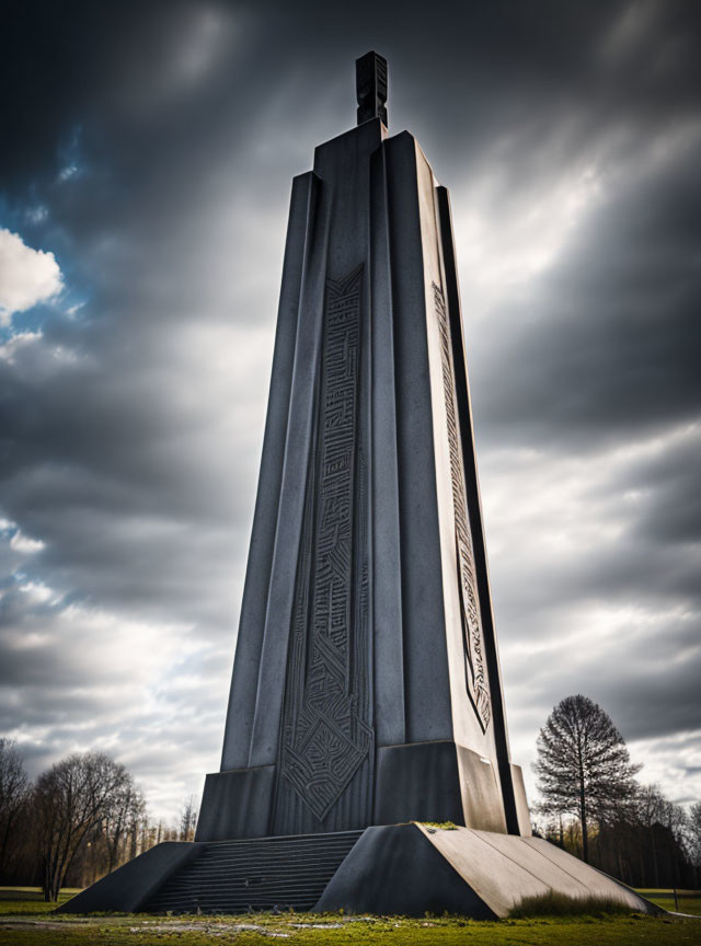 Monument with intricate etchings and solitary tree under cloudy skies