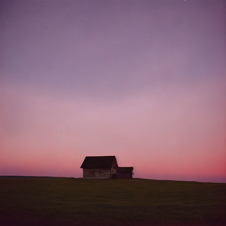 Wooden house on vast field under twilight sky with stars.