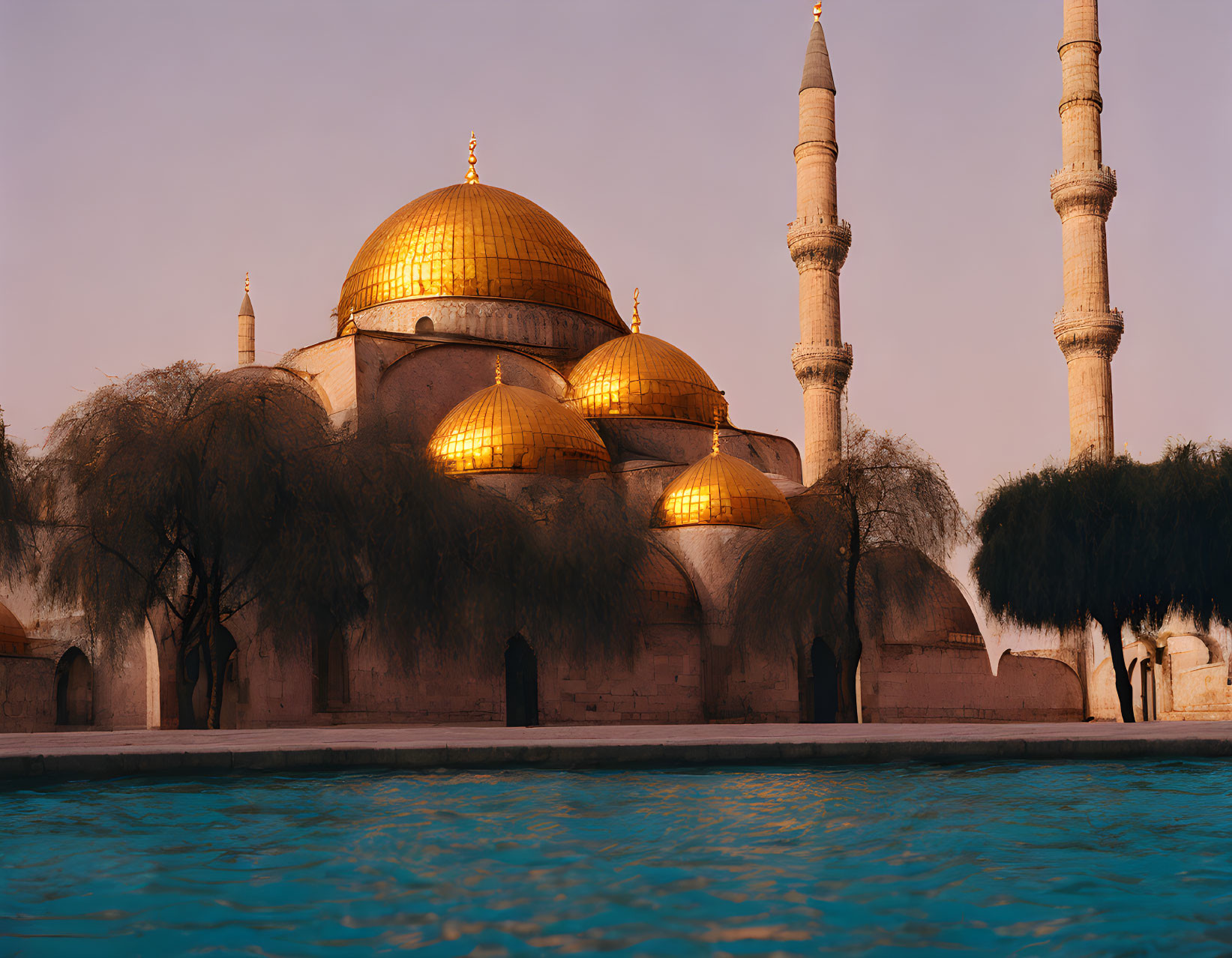 Historic mosque with golden domes and minarets at sunset by tranquil waters