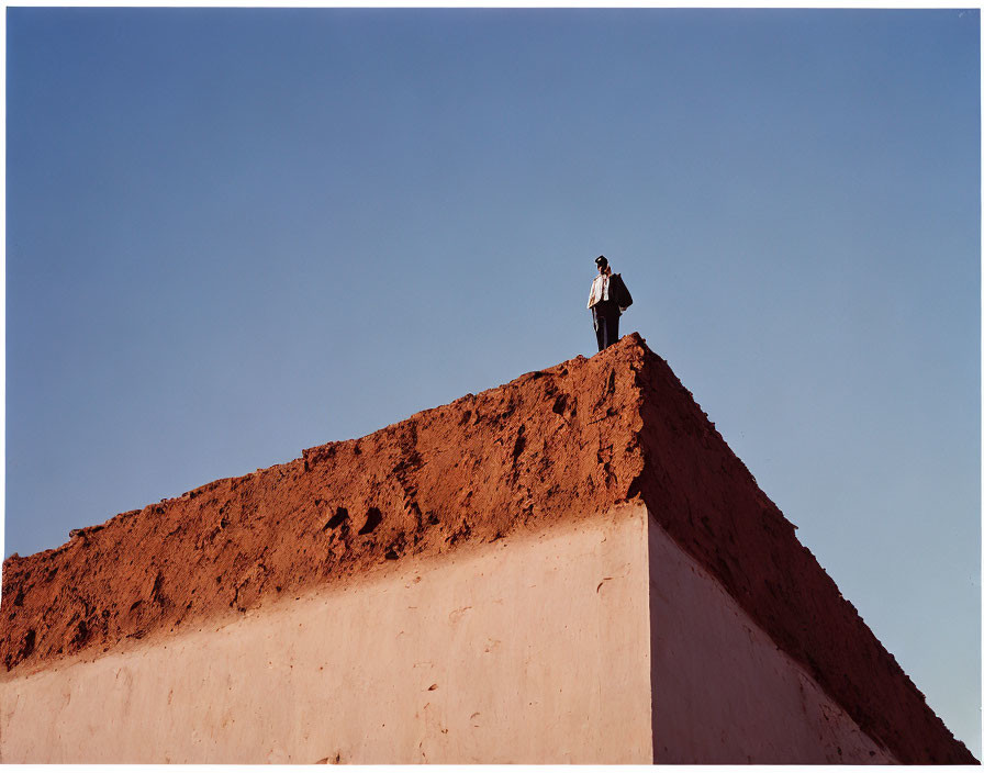 Person standing on high red clay wall against clear blue sky