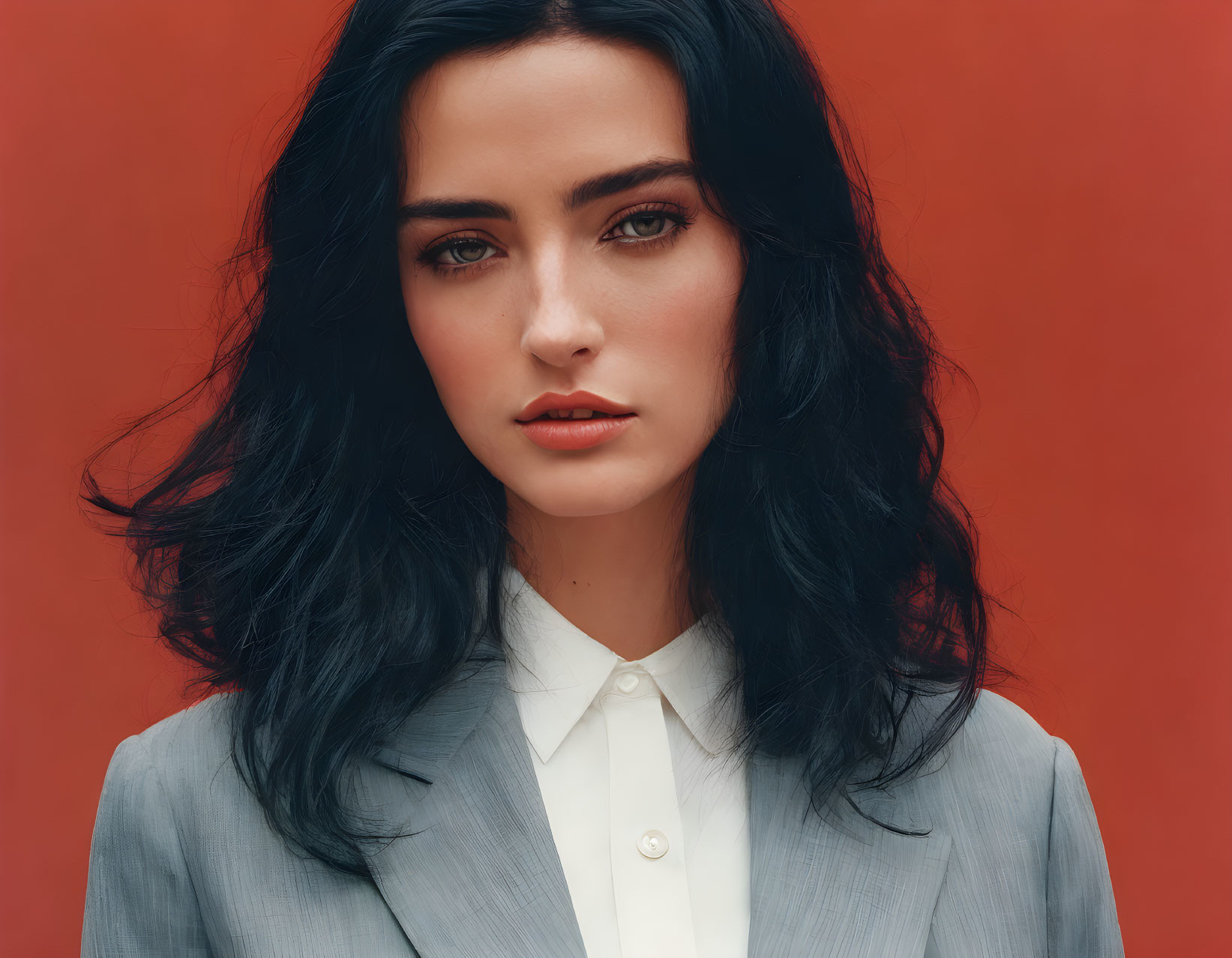 Dark-haired woman in grey blazer on red background gazes at camera