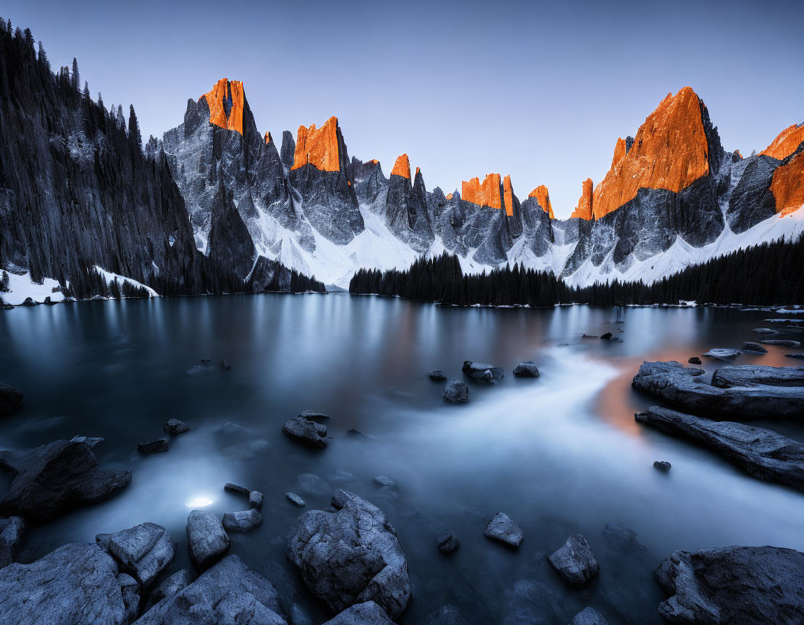 Tranquil mountain lake at twilight with glowing orange peaks