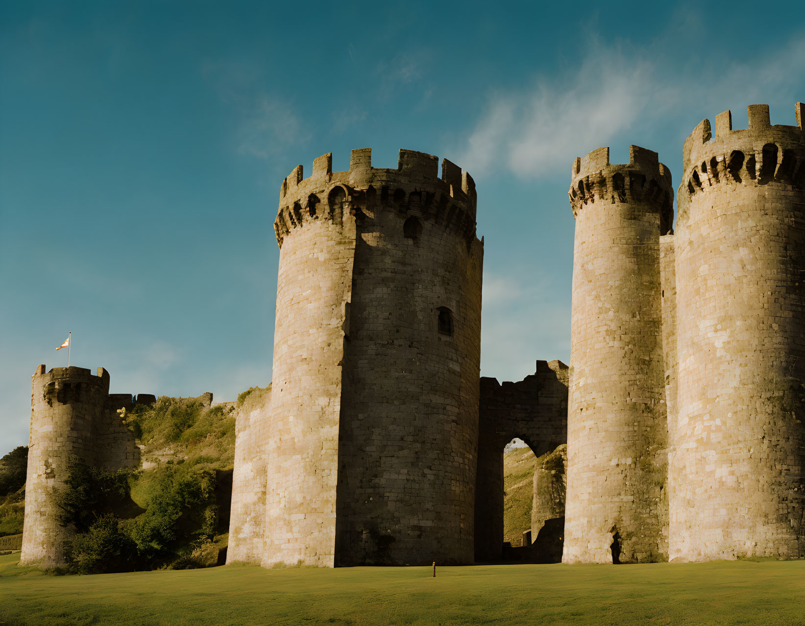 Medieval stone castle with three towers and battlements against clear blue sky.