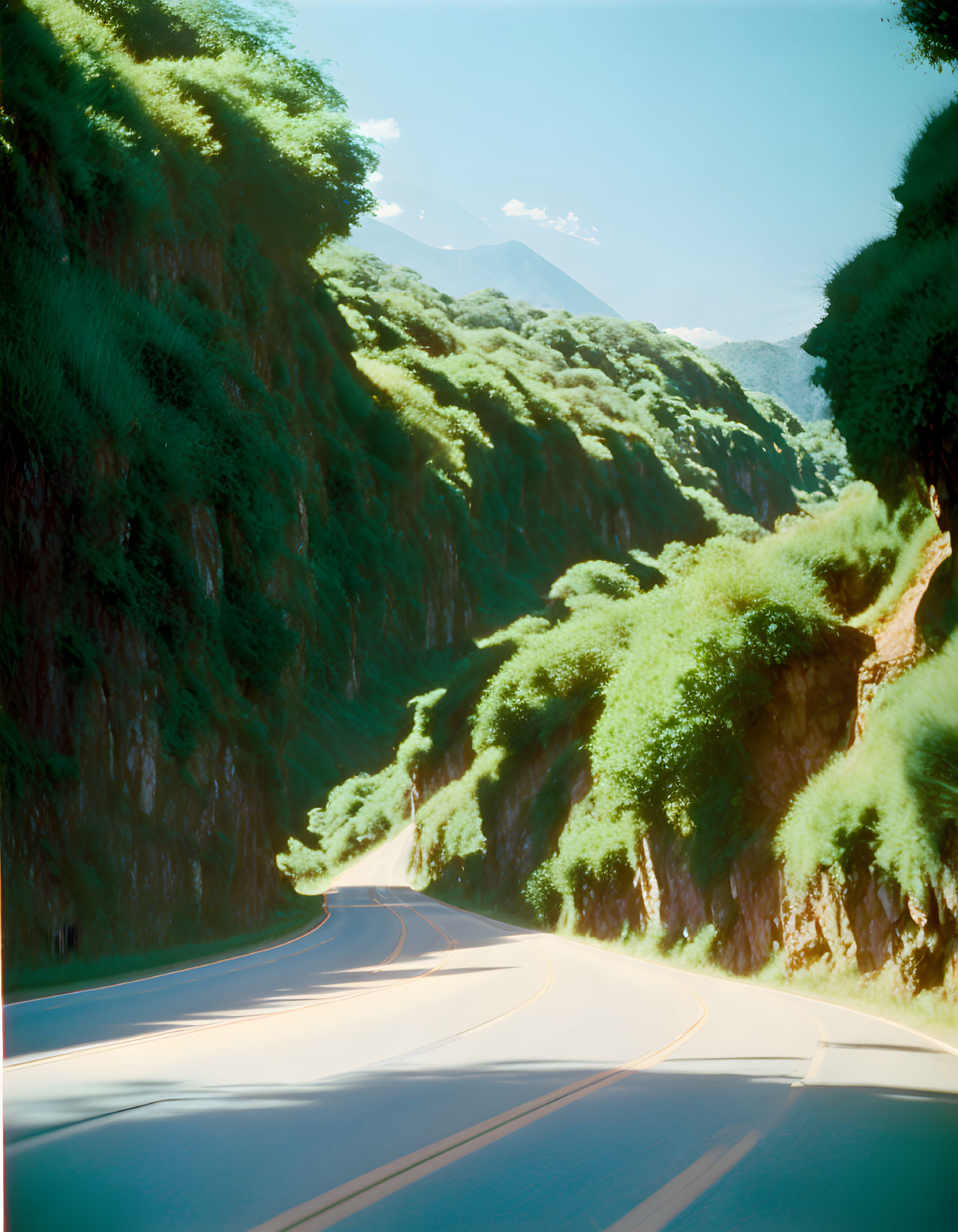 Scenic image of winding road through green hills under blue sky