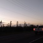 Stylized car on road at dusk with sunset behind trees & power lines