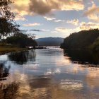 Tranquil sunset landscape with lake, trees, and mountains