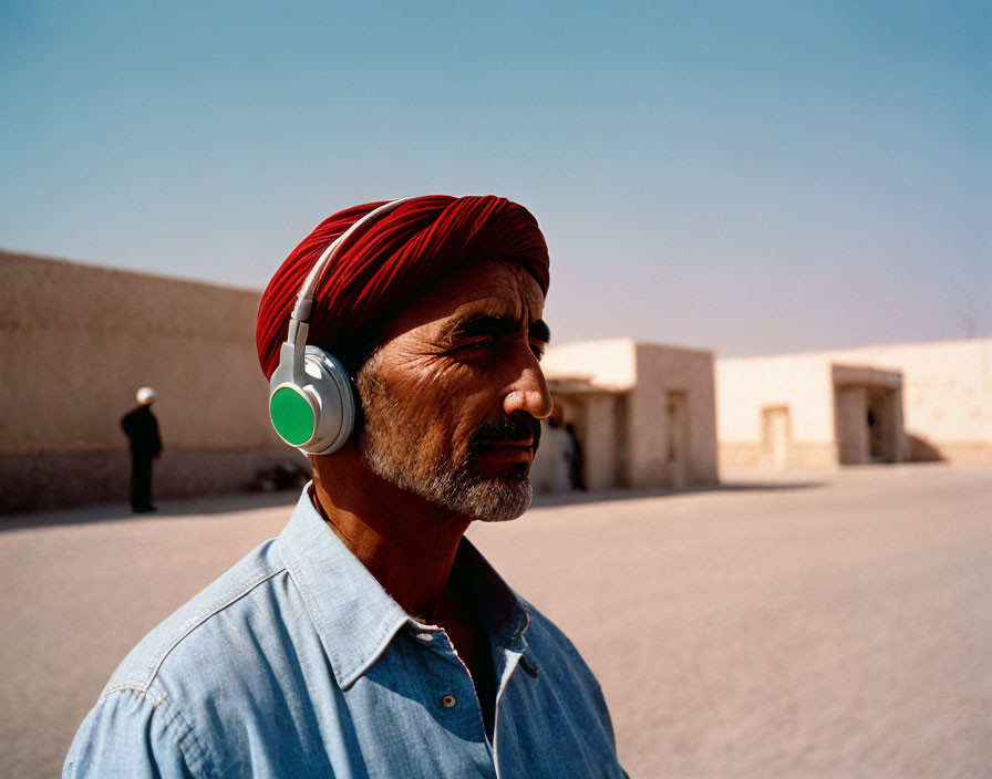 Man in red turban and headphones against clear sky and low buildings