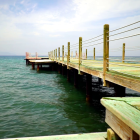 Wooden pier with rope railings extending into tranquil sea under cloudy sky.