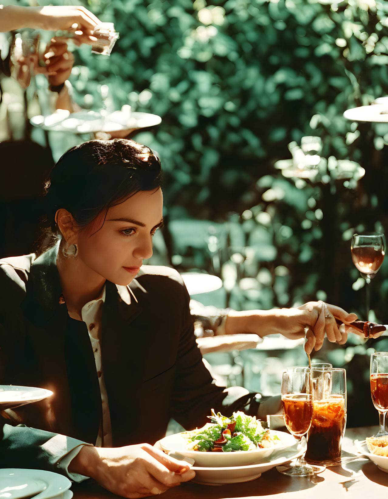 Sophisticated woman dining outdoors with waiter serving, pouring dressing on salad