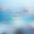 Scenic blue-green waves crashing on rocky shores with misty cliffs and flying birds under a hazy