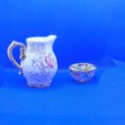 Floral-patterned white teapot and cup with gold accents on blue background with pink petals