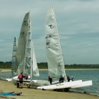 Sailboats on shimmering waters near coastal village with artistic sky.