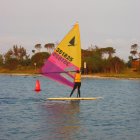 Colorful sailboat on calm water with autumn trees and other boats in the background