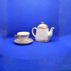 Porcelain teapot, cup, and glass vase with floral design on blue background