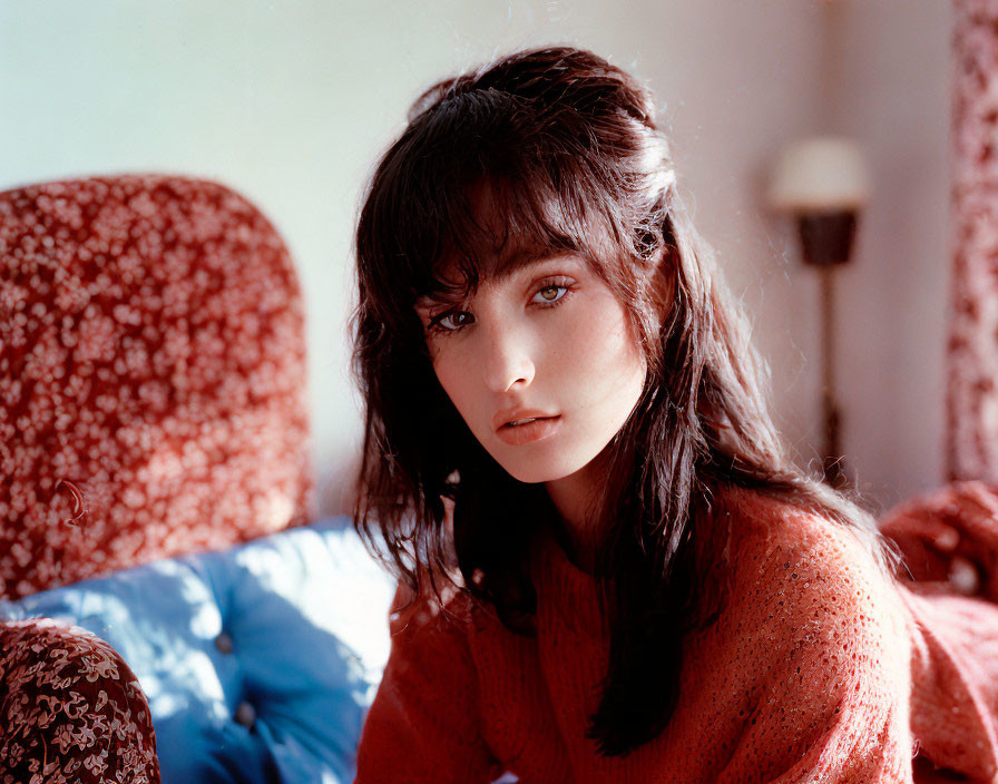 Dark-haired person in red sweater with bangs seated indoors in daylight