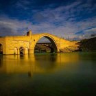 Woman in flowing dress on ornate yellow bridge over serene river