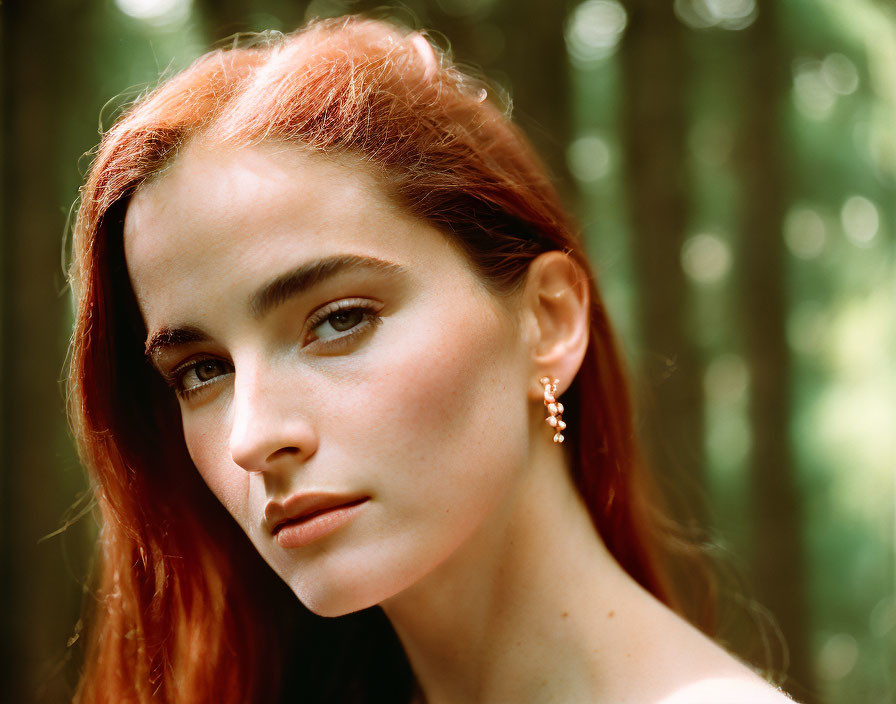 Red-haired woman with earring against greenery background