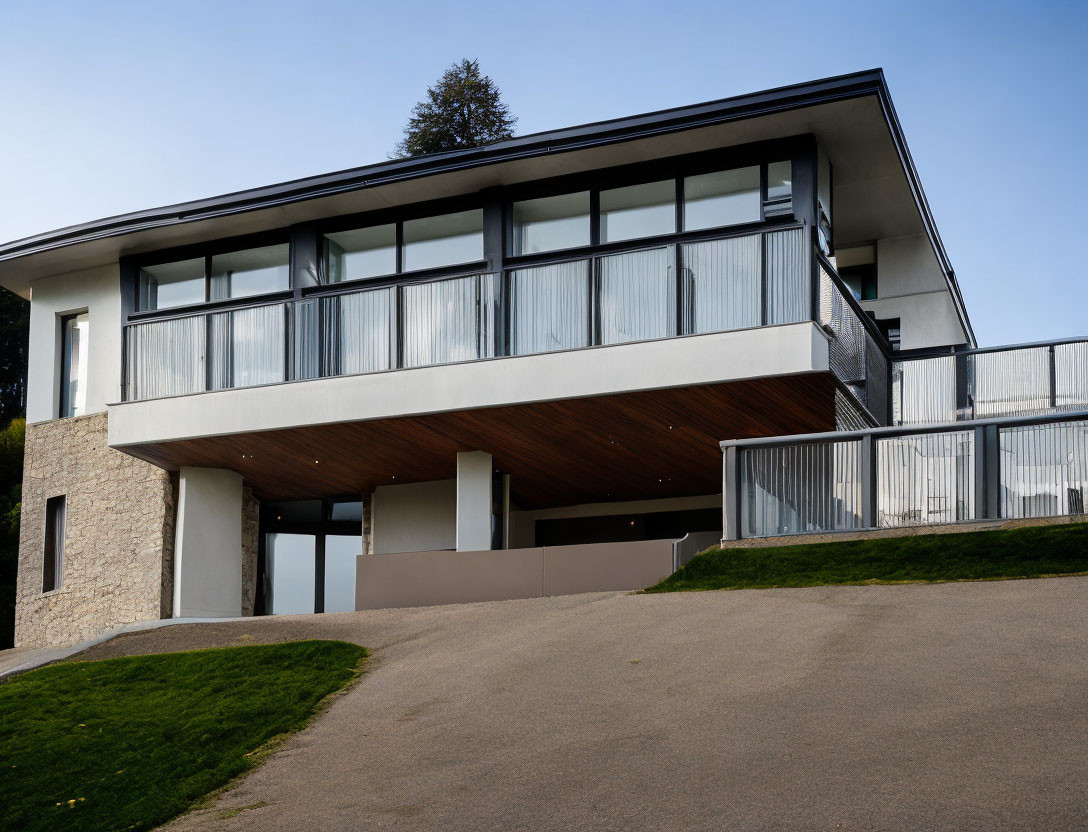 Contemporary two-story house with large windows, stone walls, balcony, and green lawn.