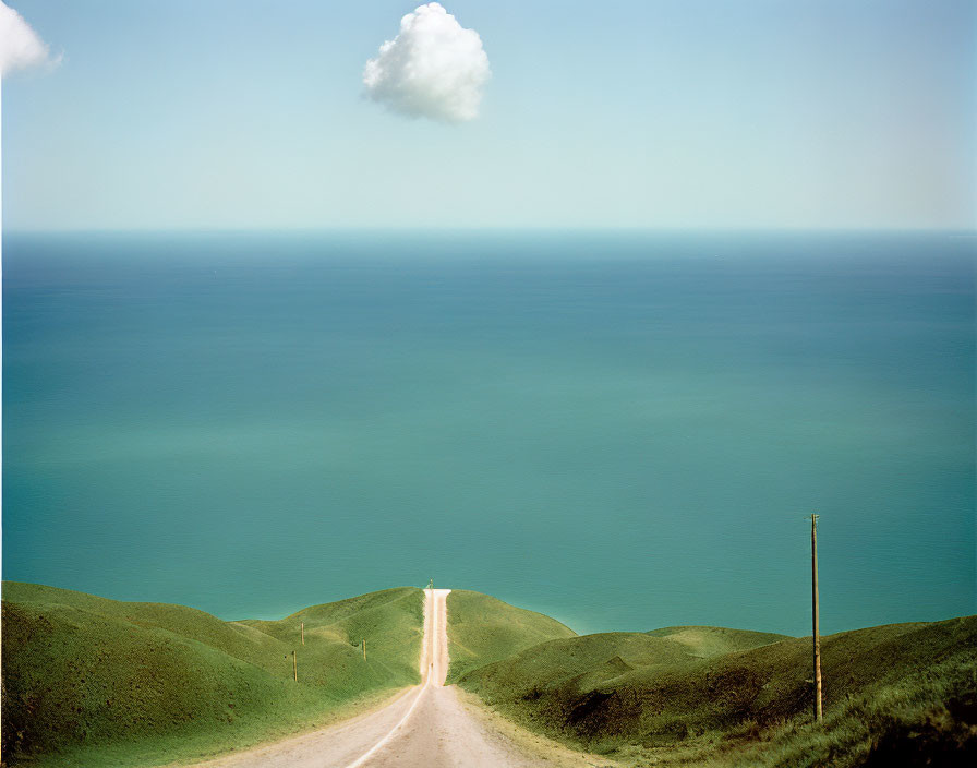 Tranquil scene: dirt road, blue sea, green hills, clear sky