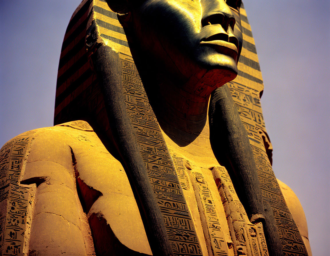 Ancient Egyptian statue with hieroglyphs and detailed face against blue sky