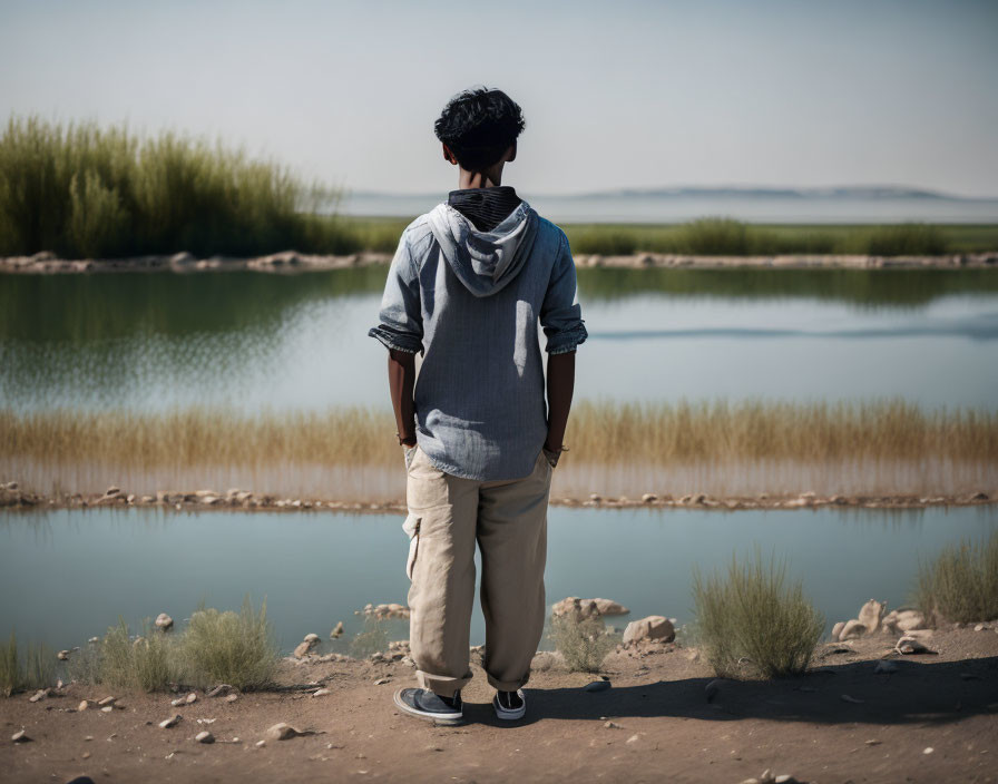 Person in Sweater Standing by Tranquil Lake with Green Reeds