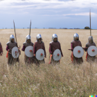 Armored warriors with shields and spears in desert landscape.