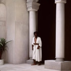 Long-Haired Person in White Robe in Elegant Arched Corridor