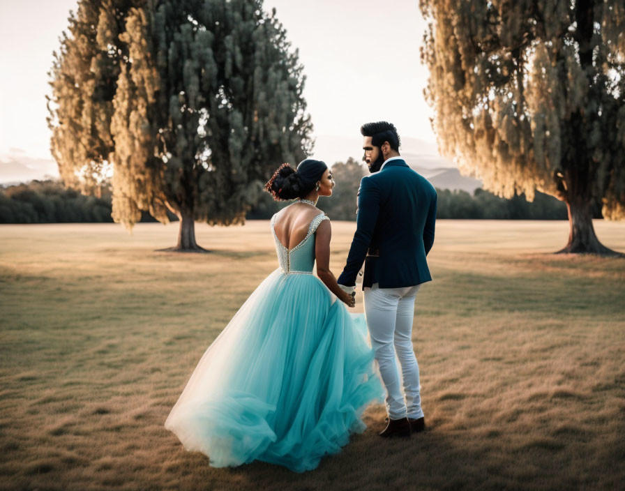 Couple in elegant attire holding hands in a field at sunset